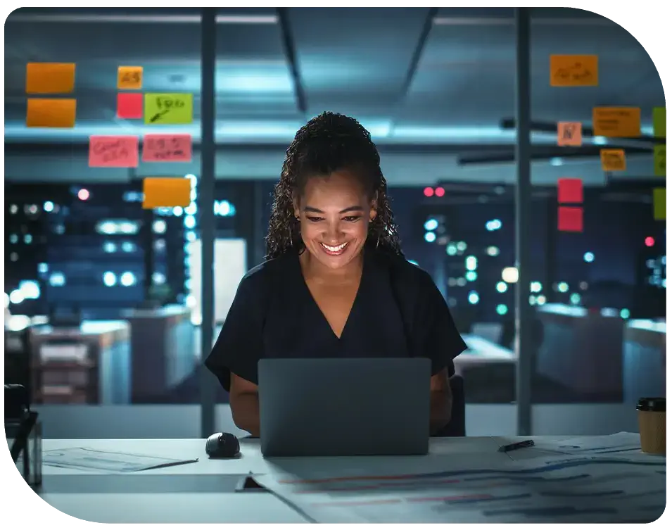 smiling woman looking at laptop in front of servers